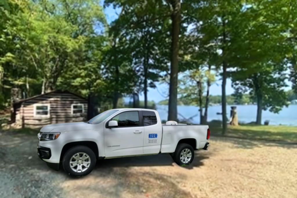 White pickup truck with KEEN logo in front of a cabin and a lake.